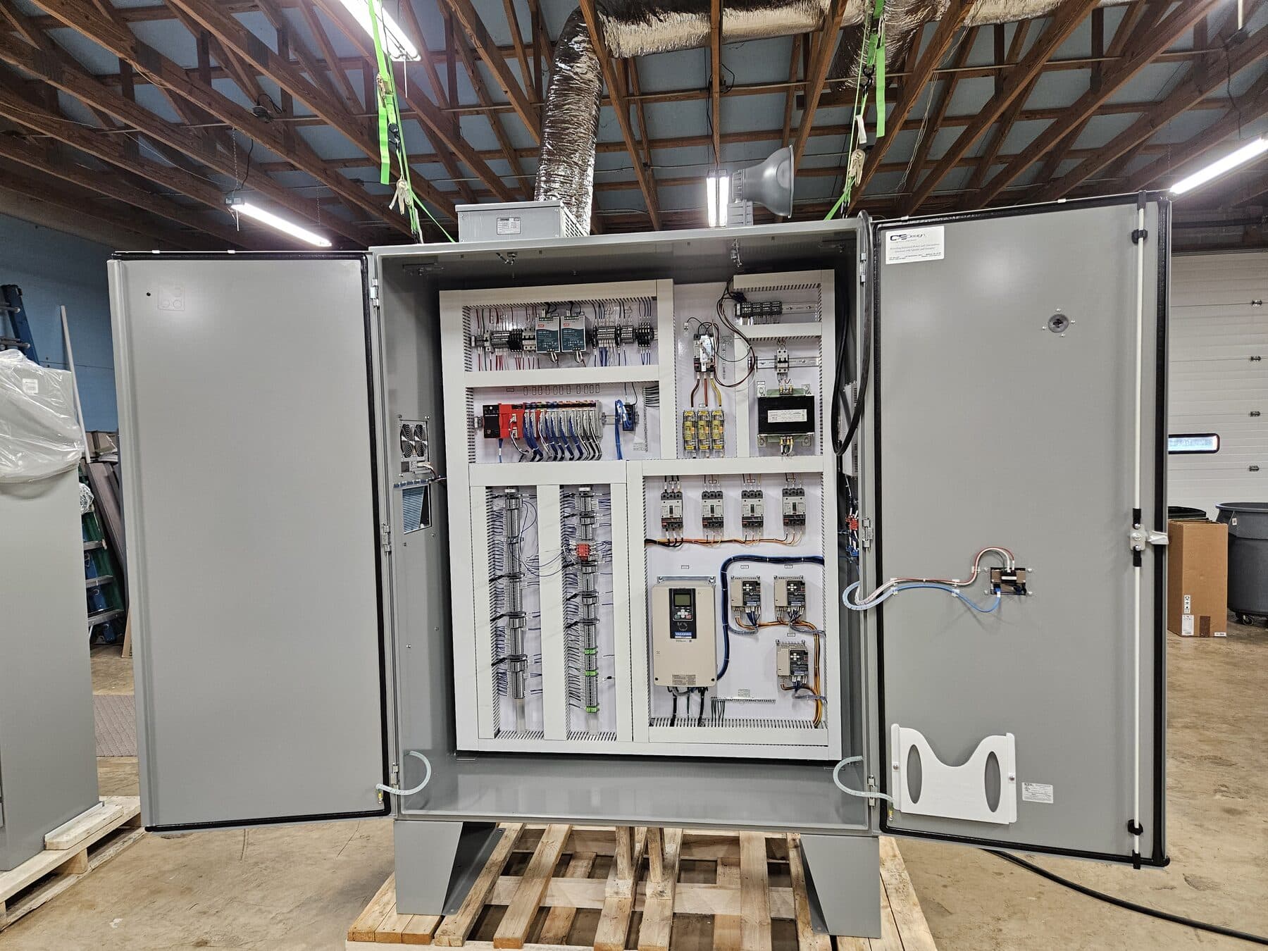 Freestanding two-door industrial control panel containing a Yaskawa variable frequency drive, safety relay, distributed I/O, control transformer, and cooling fan.